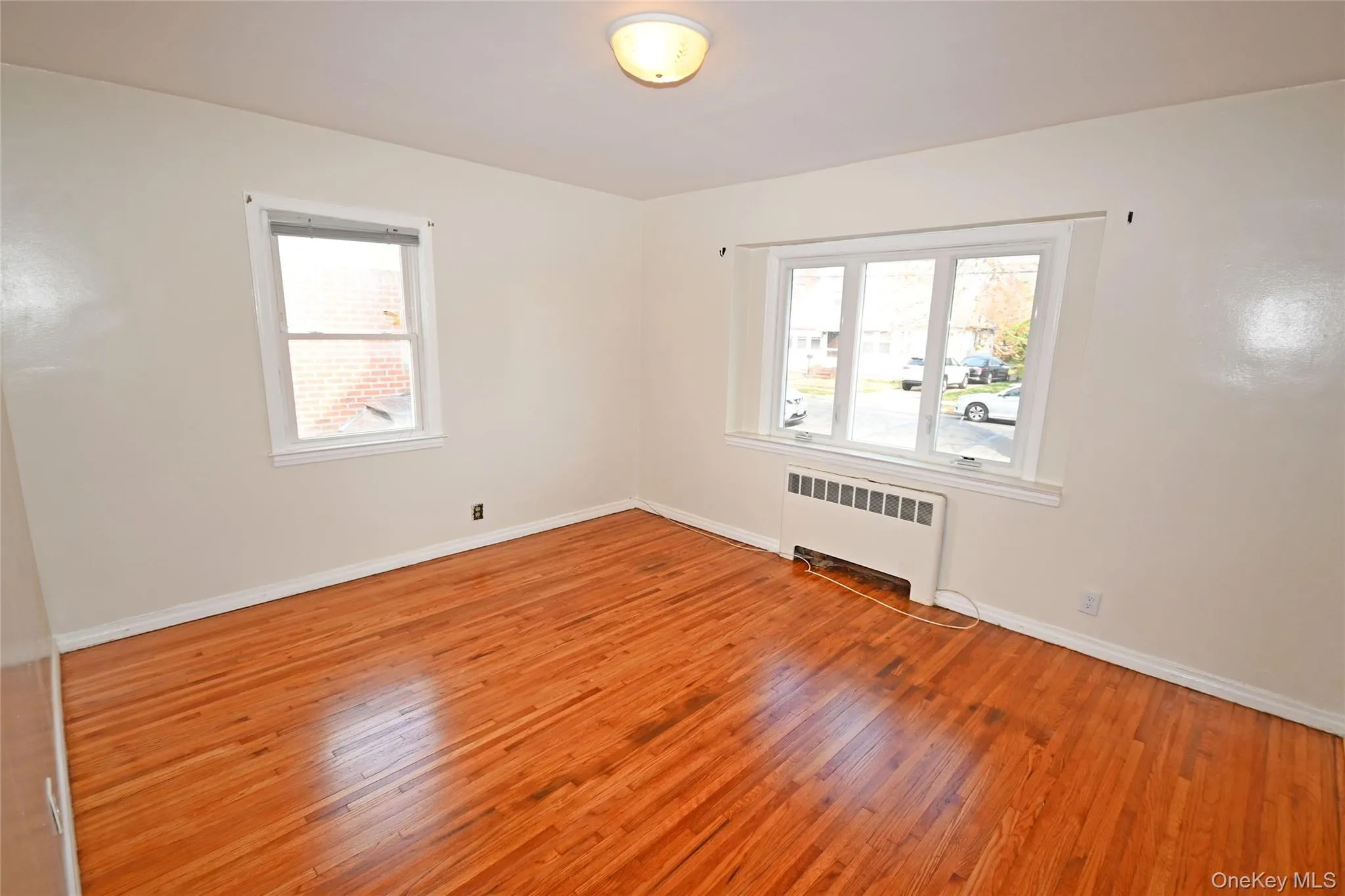 Empty room with radiator heating unit, light wood-type flooring, and plenty of natural light Empty room with radiator heating unit, light wood-type flooring, and plenty of natural light