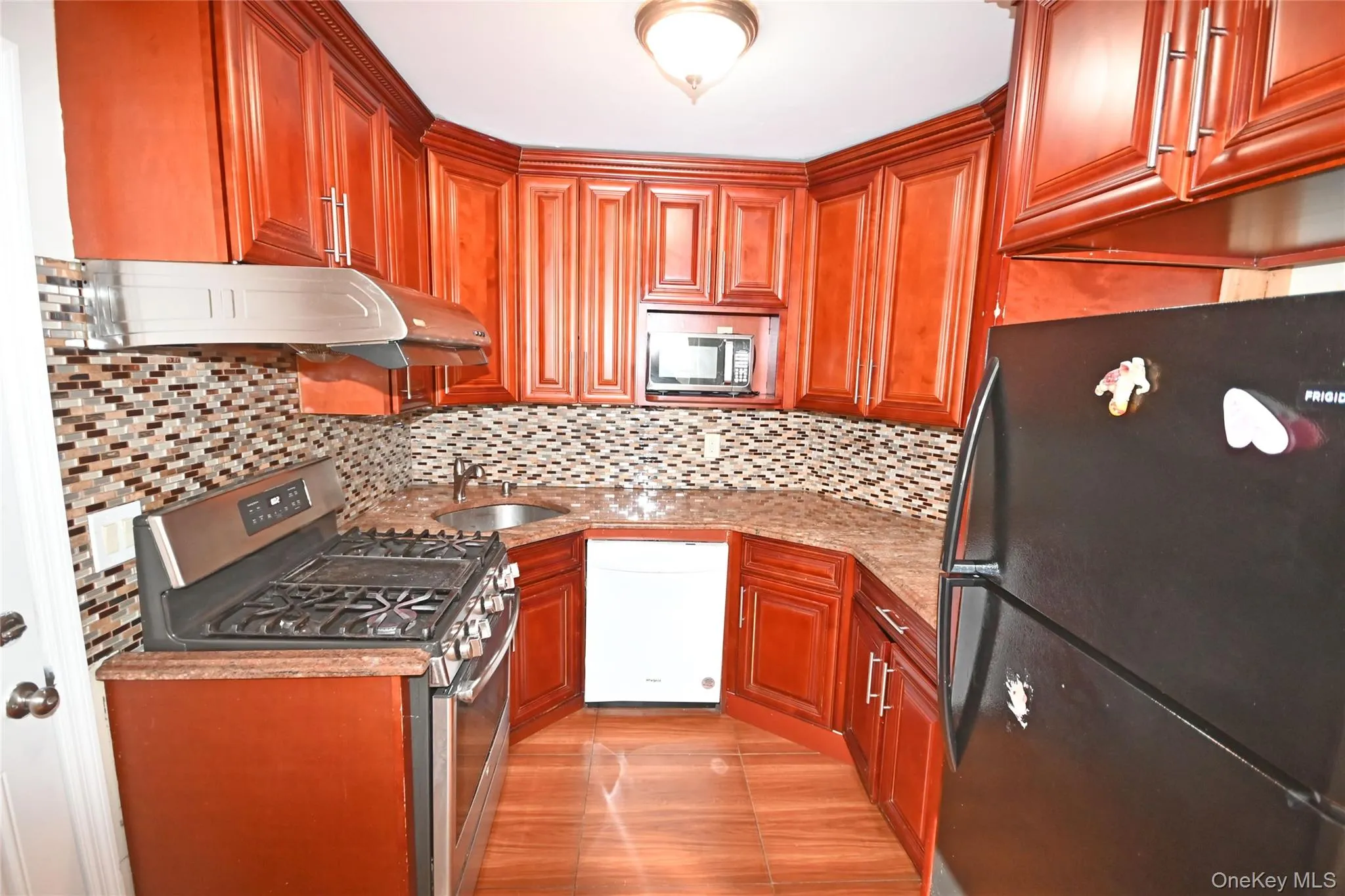 Kitchen with appliances with stainless steel finishes, light stone counters, under cabinet range hood, and brown cabinets Kitchen with appliances with stainless steel finishes, light stone counters, under cabinet range hood, and brown cabinets