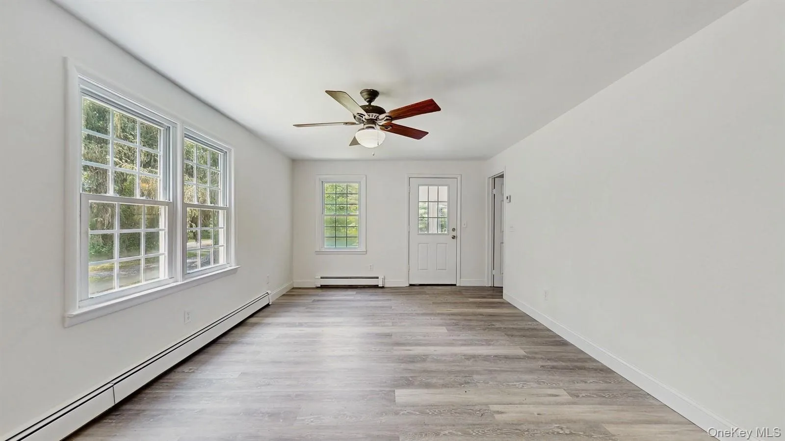 Unfurnished room with baseboard heating, light wood-style floors, and ceiling fan Unfurnished room with baseboard heating, light wood-style floors, and ceiling fan