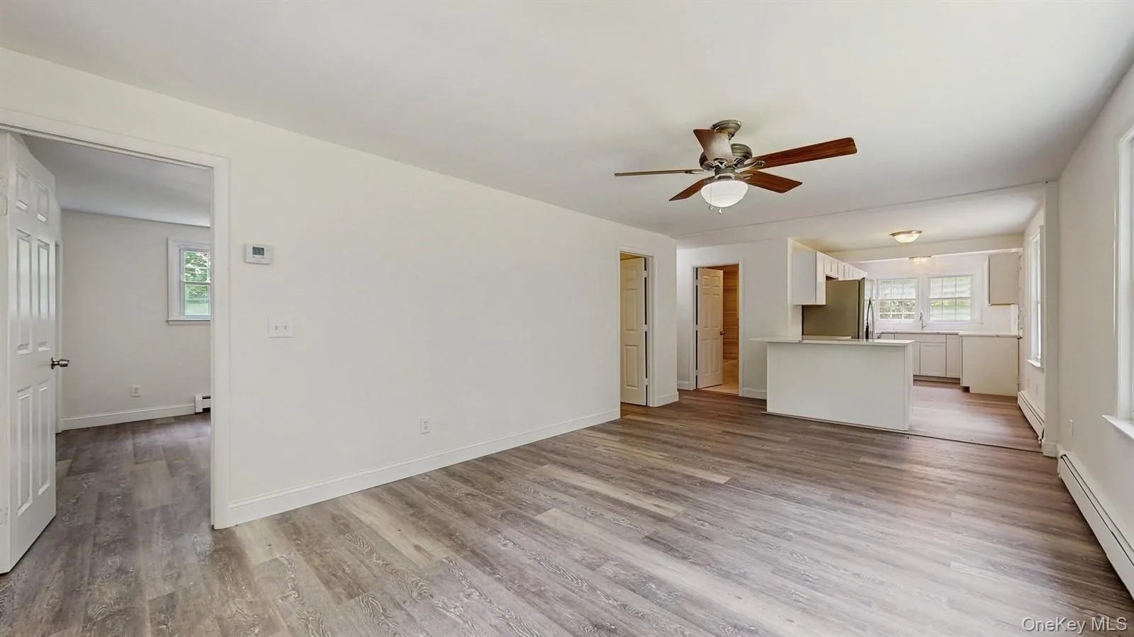 Unfurnished living room with baseboard heating, a ceiling fan, and wood finished floors Unfurnished living room with baseboard heating, a ceiling fan, and wood finished floors