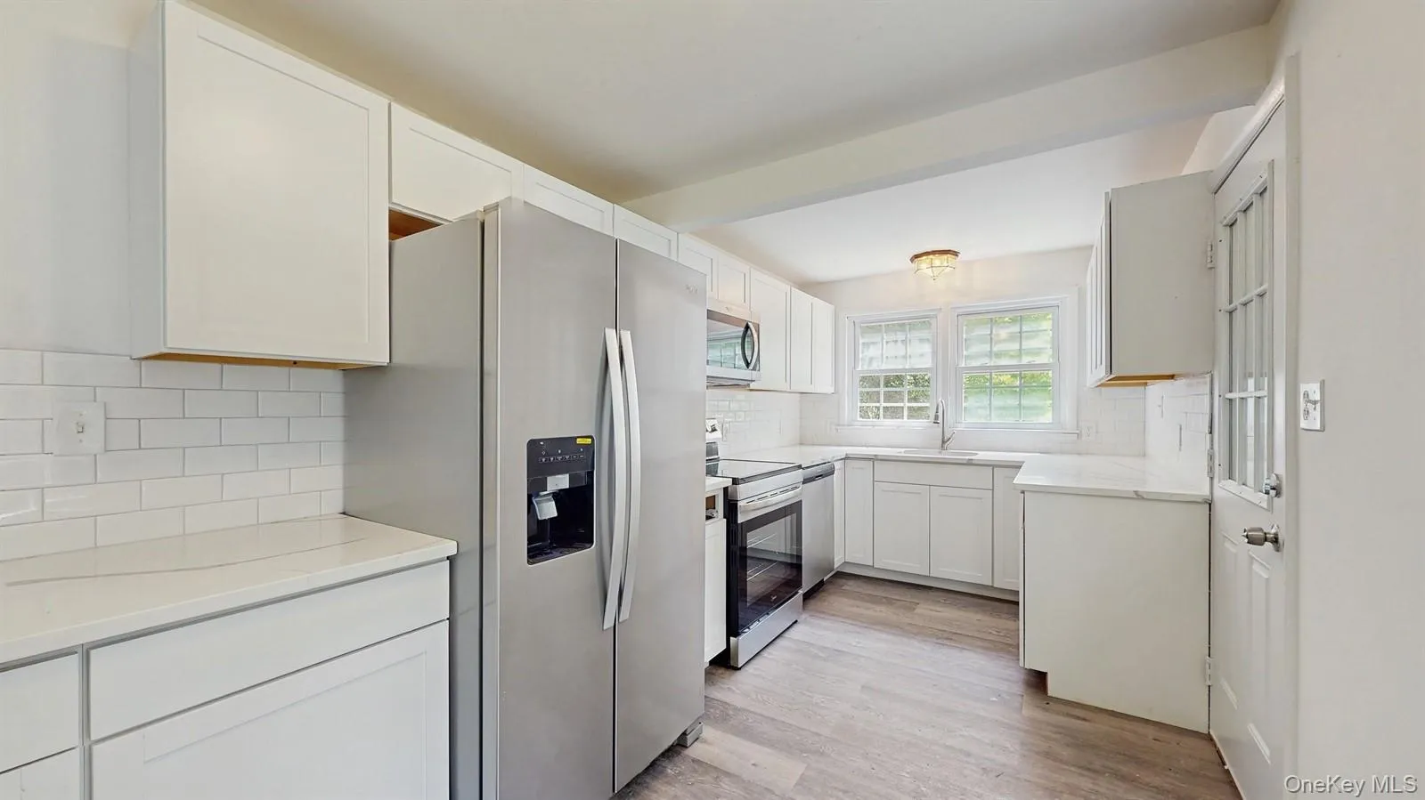 Kitchen featuring appliances with stainless steel finishes, light wood-type flooring, backsplash, and white cabinetry Kitchen featuring appliances with stainless steel finishes, light wood-type flooring, backsplash, and white cabinetry