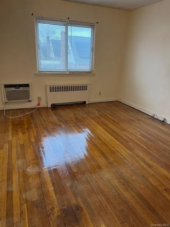 Unfurnished room featuring light wood-style flooring, radiator heating unit, and a wall mounted AC Unfurnished room featuring light wood-style flooring, radiator heating unit, and a wall mounted AC