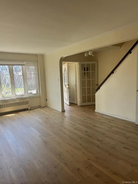 Unfurnished living room with radiator heating unit, arched walkways, wood finished floors, and stairs Unfurnished living room with radiator heating unit, arched walkways, wood finished floors, and stairs
