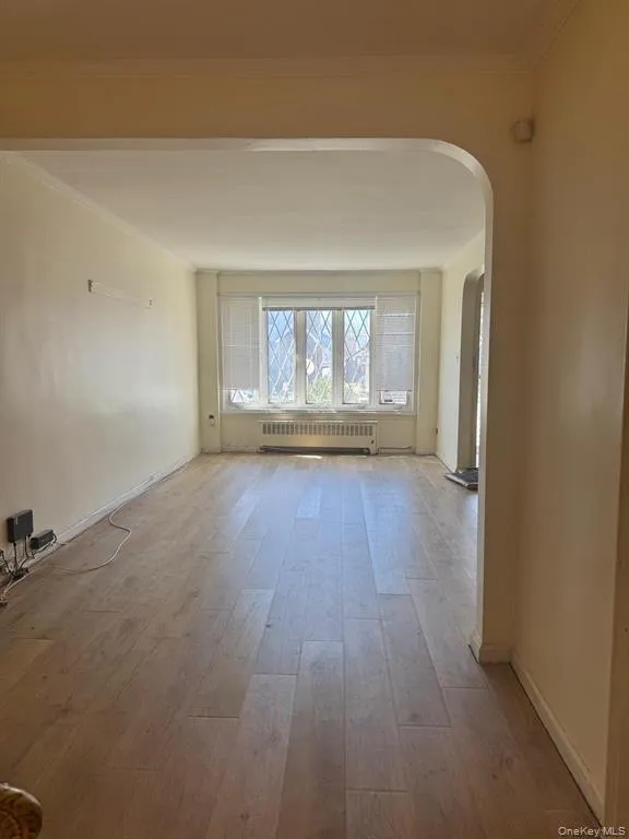 Empty room featuring arched walkways, hardwood / wood-style floors, radiator, and crown molding Empty room featuring arched walkways, hardwood / wood-style floors, radiator, and crown molding