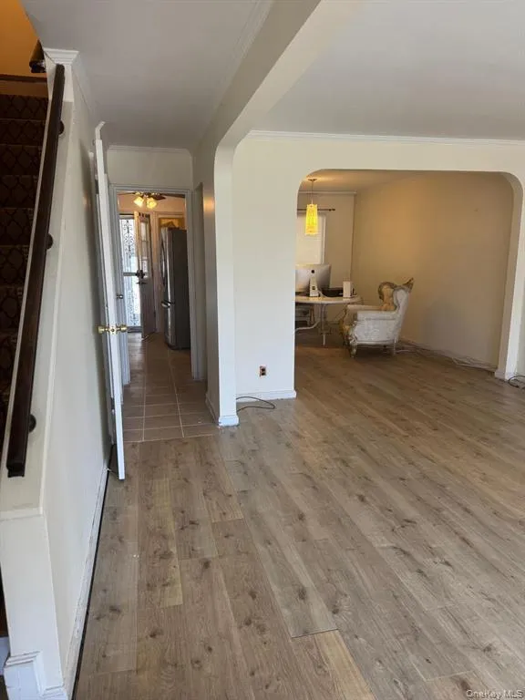 Hallway with arched walkways, light wood-type flooring, and crown molding Hallway with arched walkways, light wood-type flooring, and crown molding