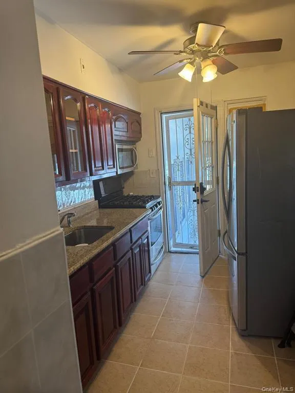Kitchen featuring stainless steel appliances, dark stone countertops, ceiling fan, light tile patterned flooring, and glass insert cabinets Kitchen featuring stainless steel appliances, dark stone countertops, ceiling fan, light tile patterned flooring, and glass insert cabinets