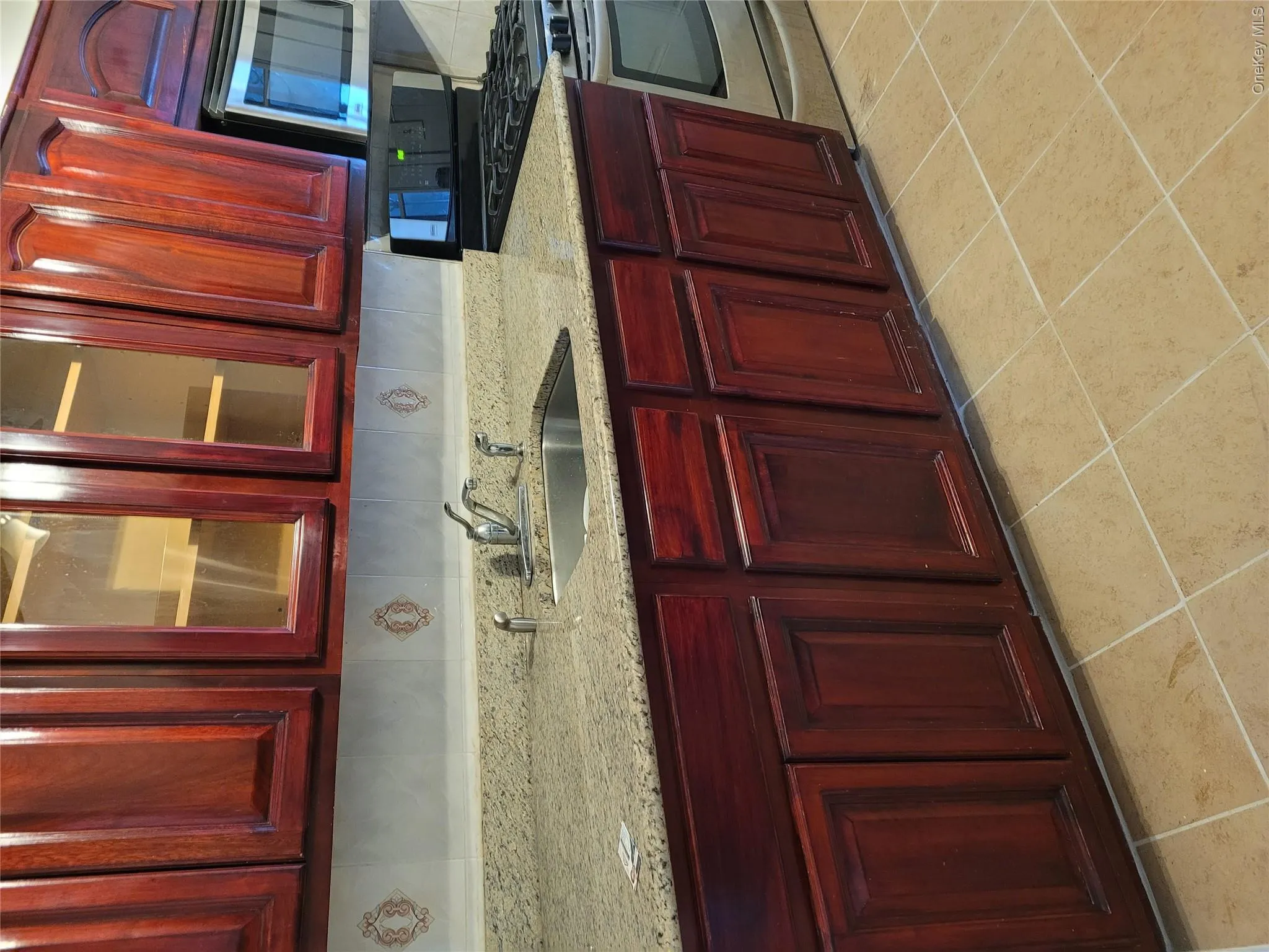 Kitchen with reddish brown cabinets, stove, light stone countertops, and glass insert cabinets Kitchen with reddish brown cabinets, stove, light stone countertops, and glass insert cabinets