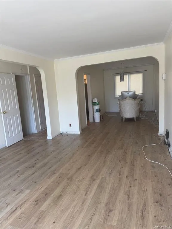 Unfurnished living room featuring arched walkways, ornamental molding, and wood finished floors Unfurnished living room featuring arched walkways, ornamental molding, and wood finished floors