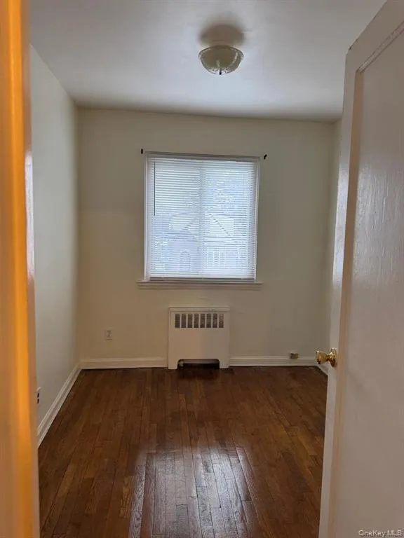 Empty room featuring radiator heating unit and dark wood-style flooring Empty room featuring radiator heating unit and dark wood-style flooring