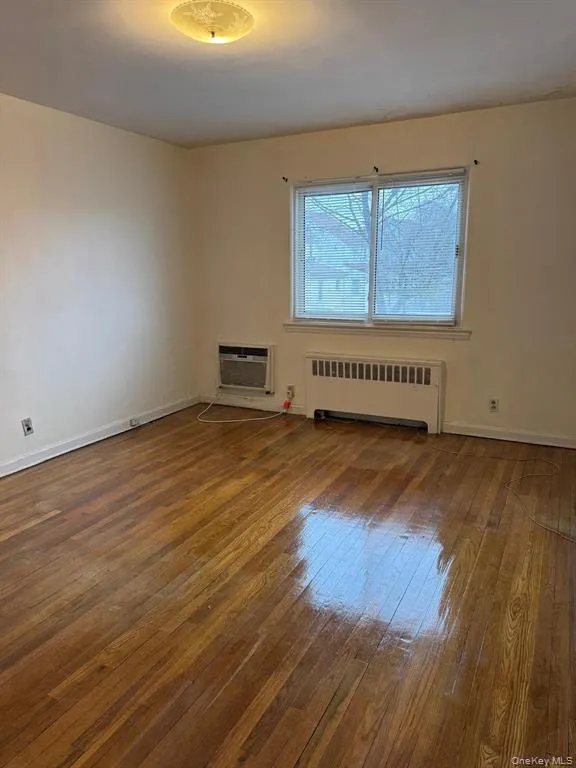 Empty room featuring radiator, dark wood finished floors, and an AC wall unit Empty room featuring radiator, dark wood finished floors, and an AC wall unit