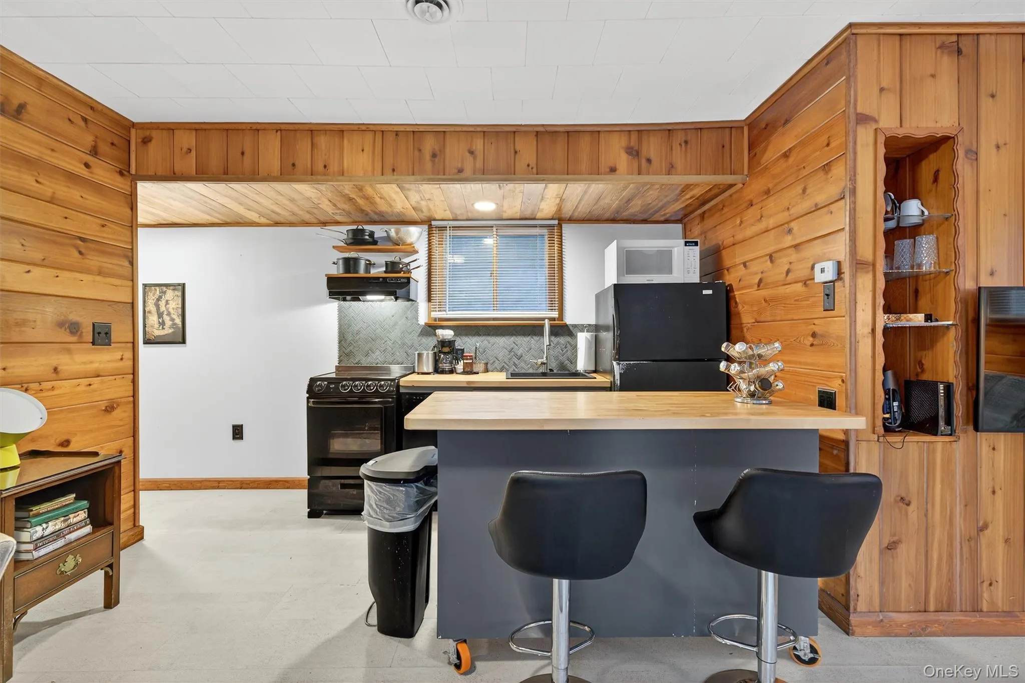 Kitchen featuring open shelves, a kitchen bar, wooden walls, black appliances, and wooden counters Kitchen featuring open shelves, a kitchen bar, wooden walls, black appliances, and wooden counters