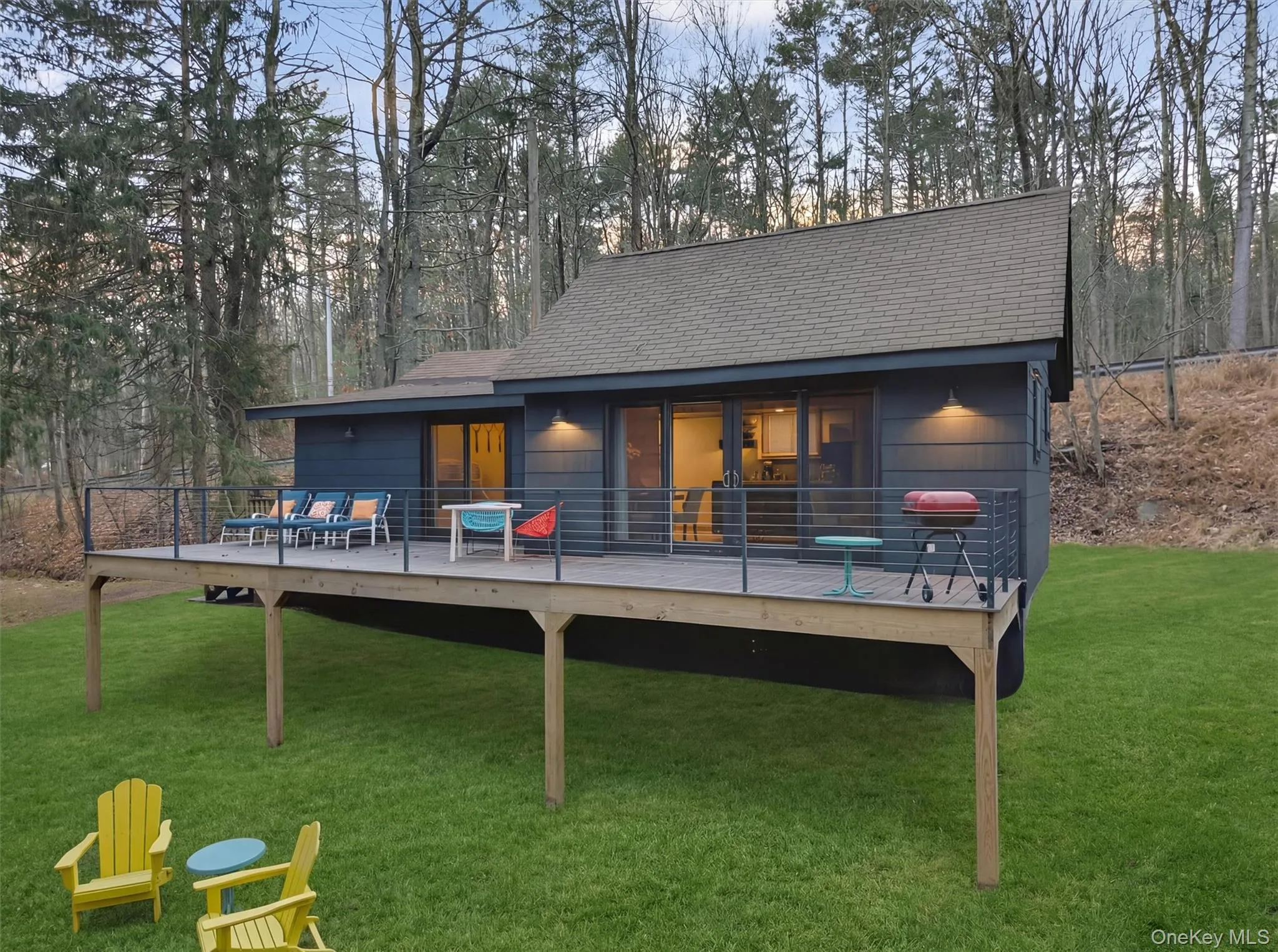 Rear view of property featuring a yard, a wooden deck, a shingled roof, and view of wooded area Rear view of property featuring a yard, a wooden deck, a shingled roof, and view of wooded area