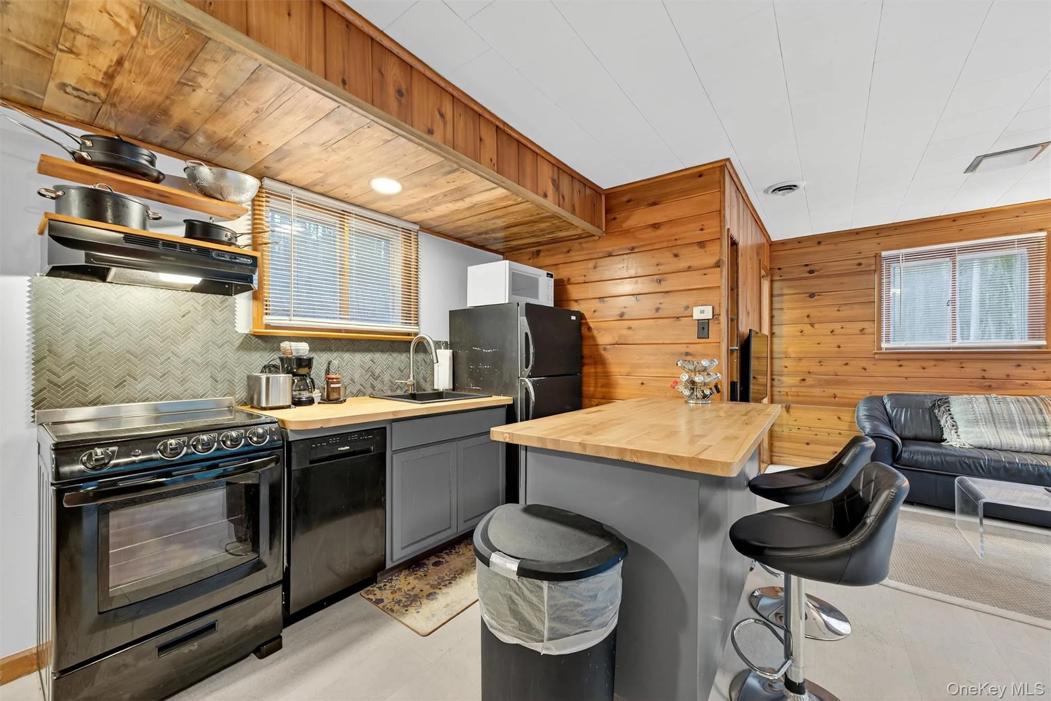 Kitchen with wood counters, black appliances, a breakfast bar, wood walls, and open floor plan Kitchen with wood counters, black appliances, a breakfast bar, wood walls, and open floor plan