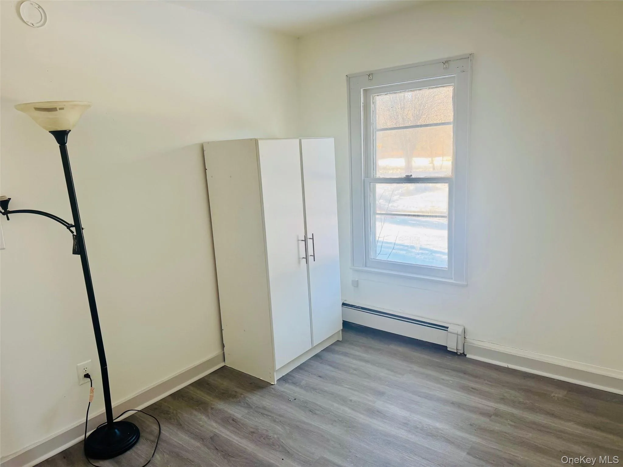 Unfurnished bedroom with a baseboard heating unit and wood finished floors Unfurnished bedroom with a baseboard heating unit and wood finished floors