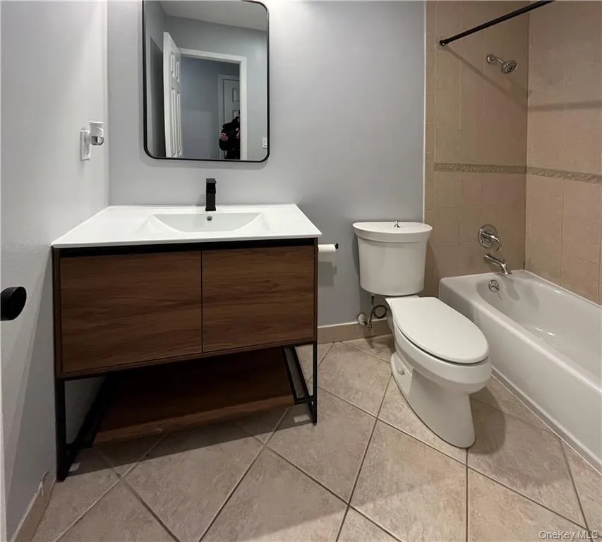 Full bath with bathtub / shower combination, tile patterned floors, toilet, vanity, and baseboards Full bath with bathtub / shower combination, tile patterned floors, toilet, vanity, and baseboards
