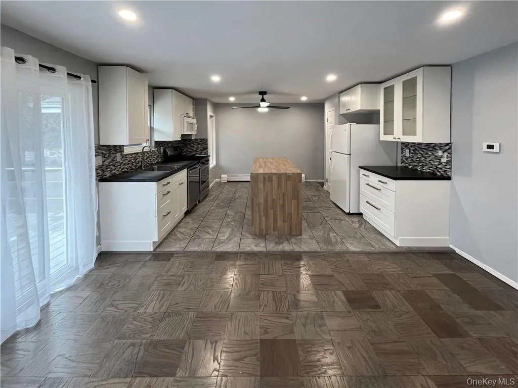 Kitchen with white appliances, a center island, a sink, a ceiling fan, and baseboard heating Kitchen with white appliances, a center island, a sink, a ceiling fan, and baseboard heating