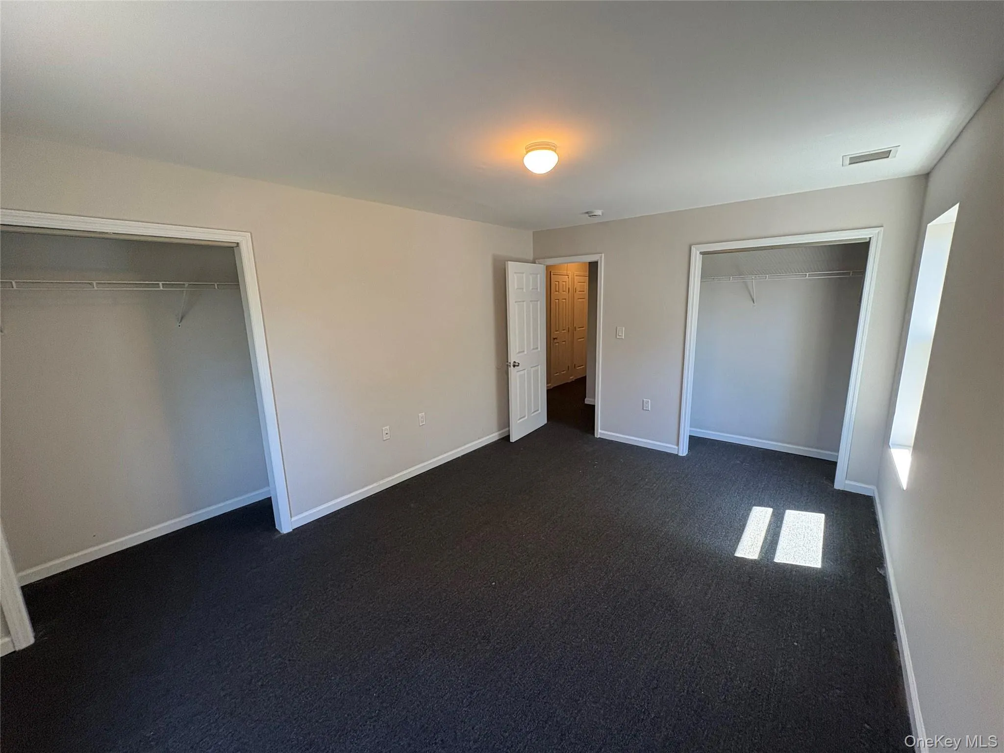 Unfurnished bedroom with dark carpet and multiple closets Unfurnished bedroom with dark carpet and multiple closets