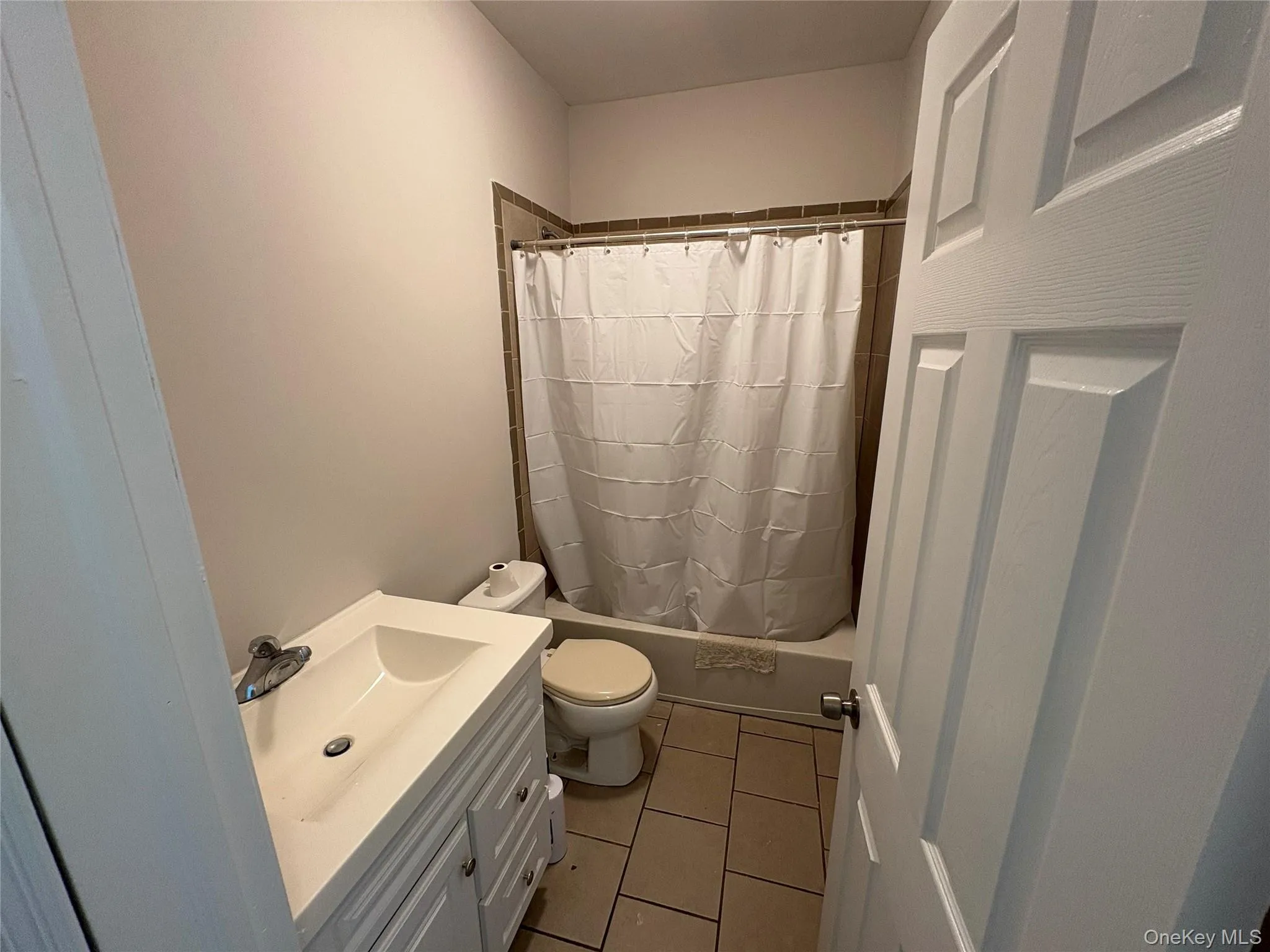 Full bath featuring vanity, light tile patterned flooring, and shower / bath combo with shower curtain Full bath featuring vanity, light tile patterned flooring, and shower / bath combo with shower curtain