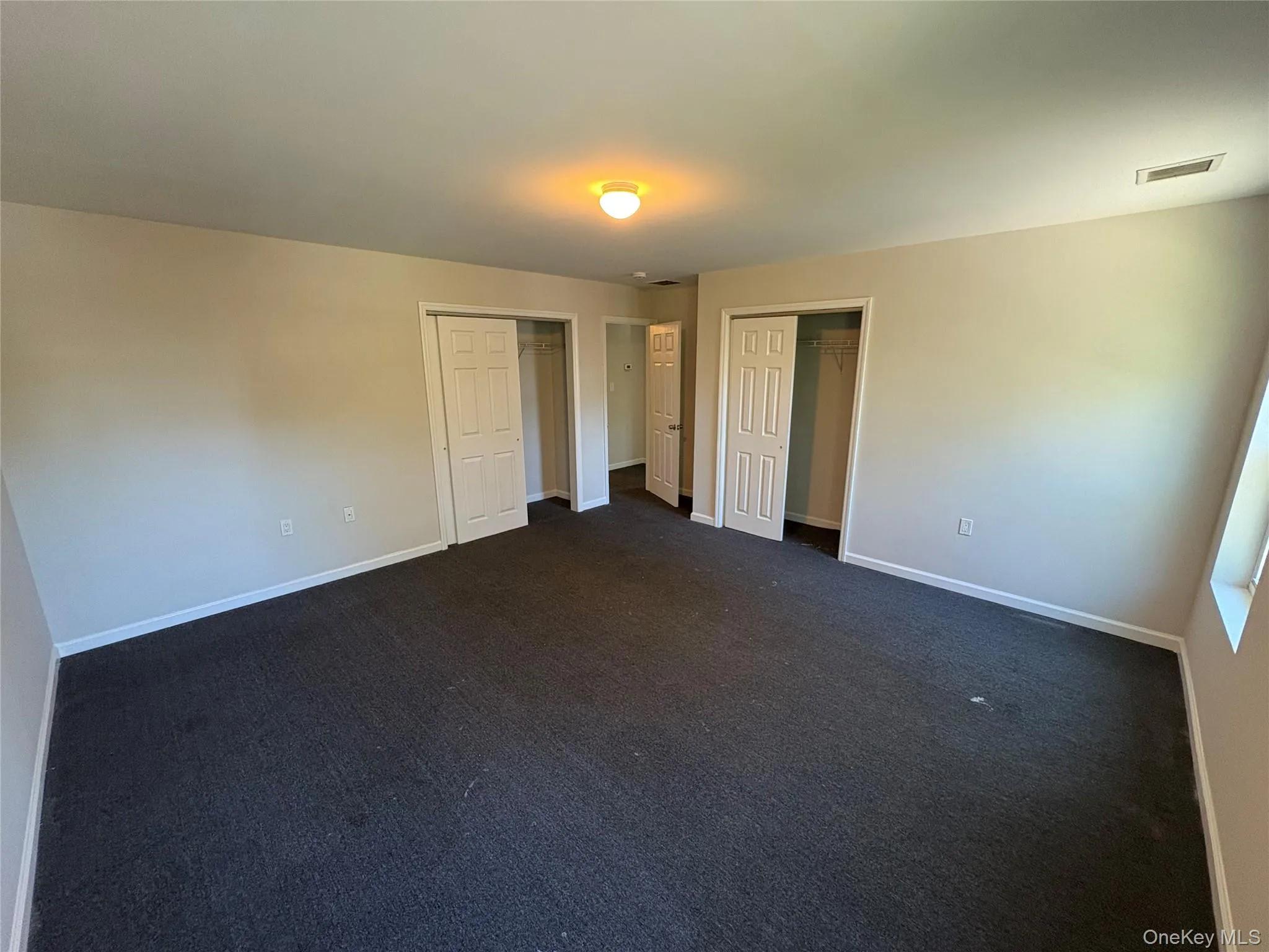 Unfurnished bedroom featuring two closets and dark colored carpet Unfurnished bedroom featuring two closets and dark colored carpet