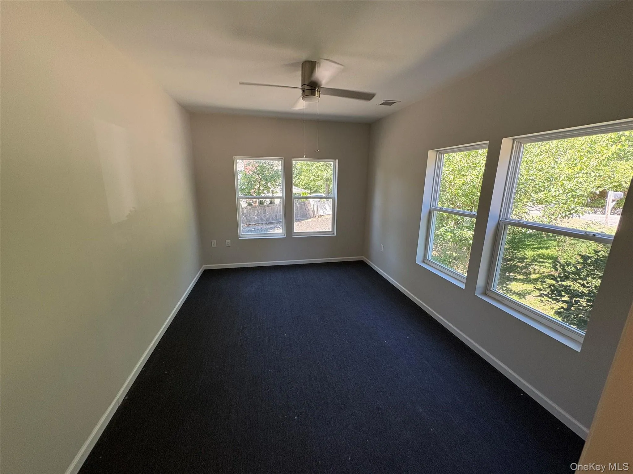 Unfurnished room featuring dark carpet and a ceiling fan Unfurnished room featuring dark carpet and a ceiling fan