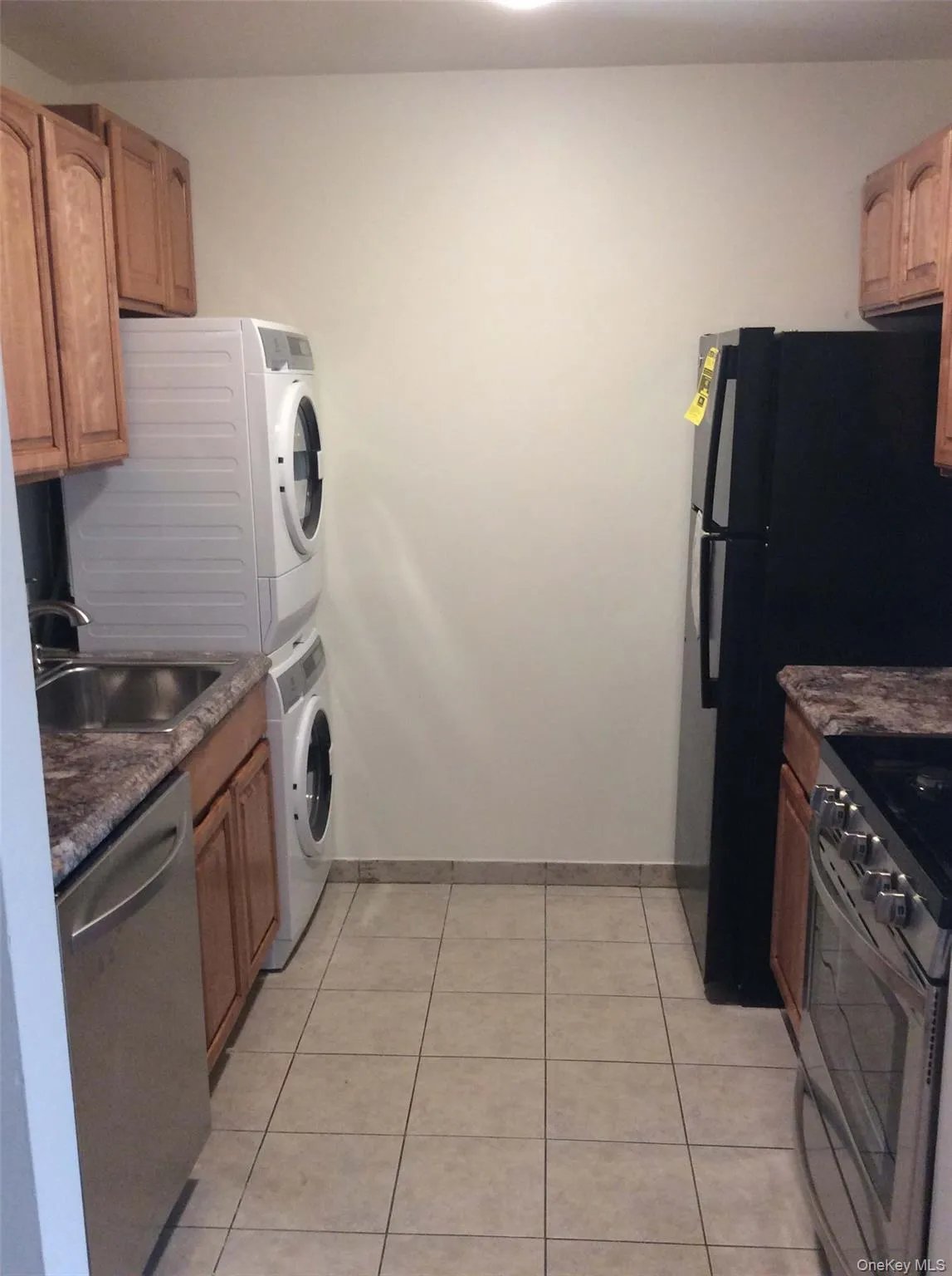 Kitchen featuring stainless steel appliances, light tile patterned floors, dark stone counters, and stacked washer / drying machine Kitchen featuring stainless steel appliances, light tile patterned floors, dark stone counters, and stacked washer / drying machine
