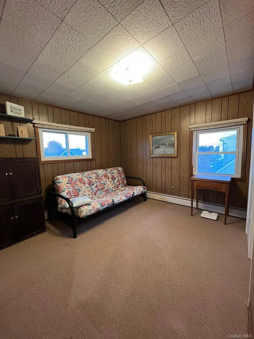 Bedroom featuring wood walls, a baseboard radiator, and light colored carpet Bedroom featuring wood walls, a baseboard radiator, and light colored carpet