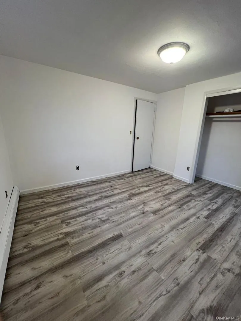 Unfurnished bedroom featuring baseboard heating, a closet, and wood finished floors Unfurnished bedroom featuring baseboard heating, a closet, and wood finished floors