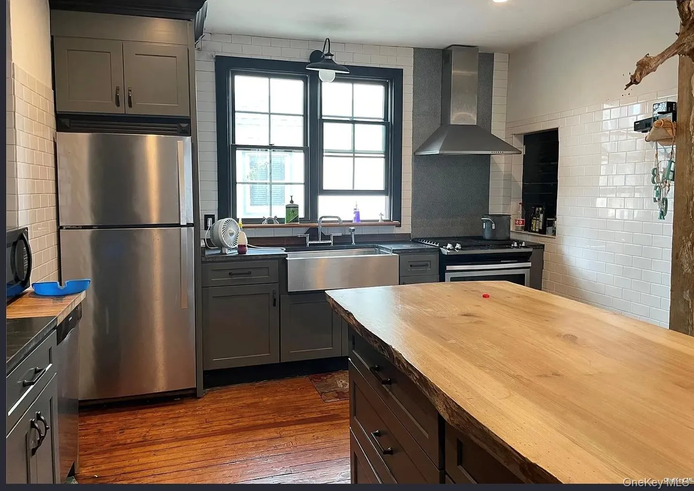 Kitchen with stainless steel appliances, wall chimney exhaust hood, dark wood-style flooring, and gray cabinetry Kitchen with stainless steel appliances, wall chimney exhaust hood, dark wood-style flooring, and gray cabinetry