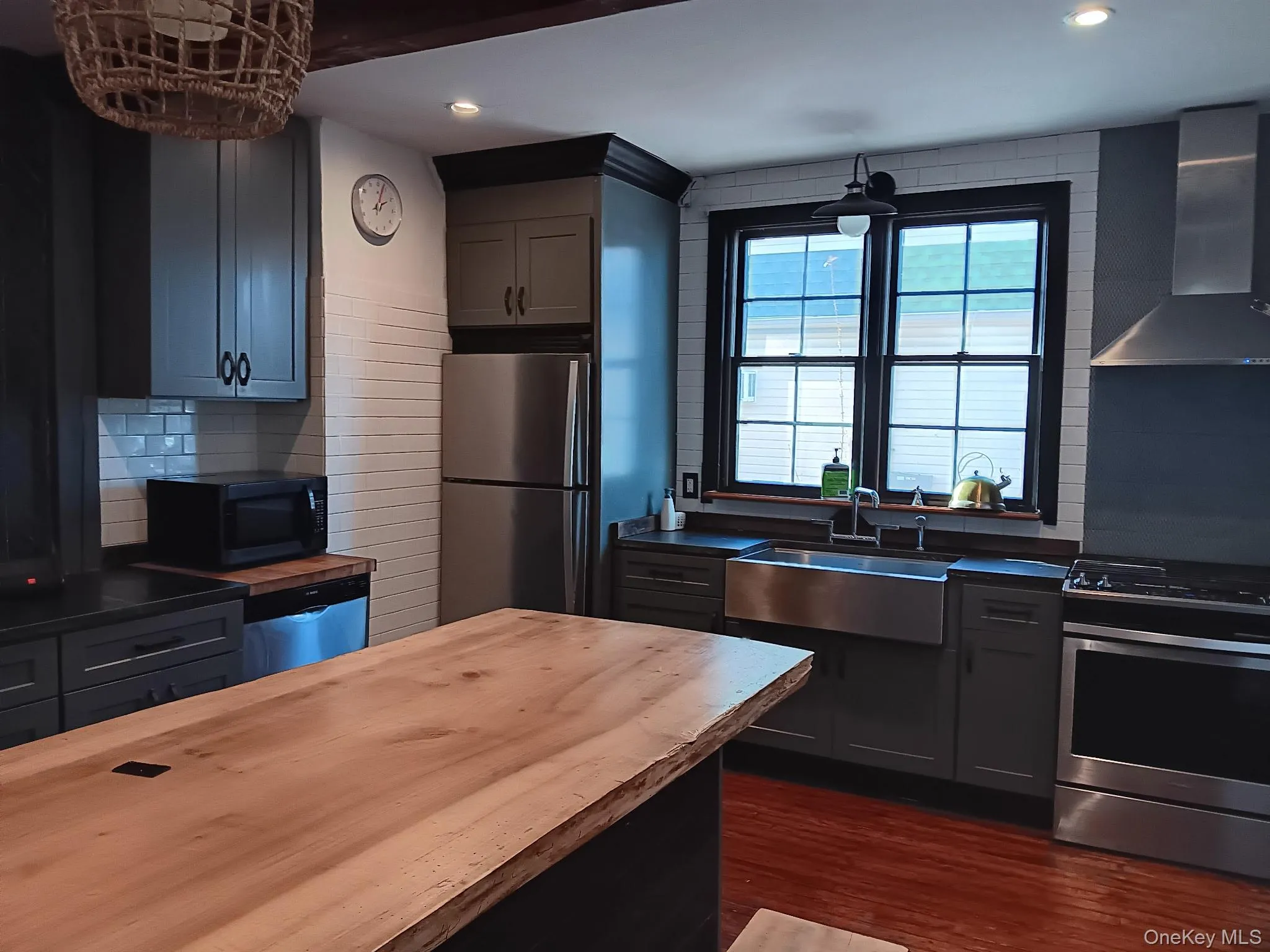 Kitchen featuring wall chimney range hood, appliances with stainless steel finishes, decorative backsplash, dark wood-type flooring, and wood counters Kitchen featuring wall chimney range hood, appliances with stainless steel finishes, decorative backsplash, dark wood-type flooring, and wood counters