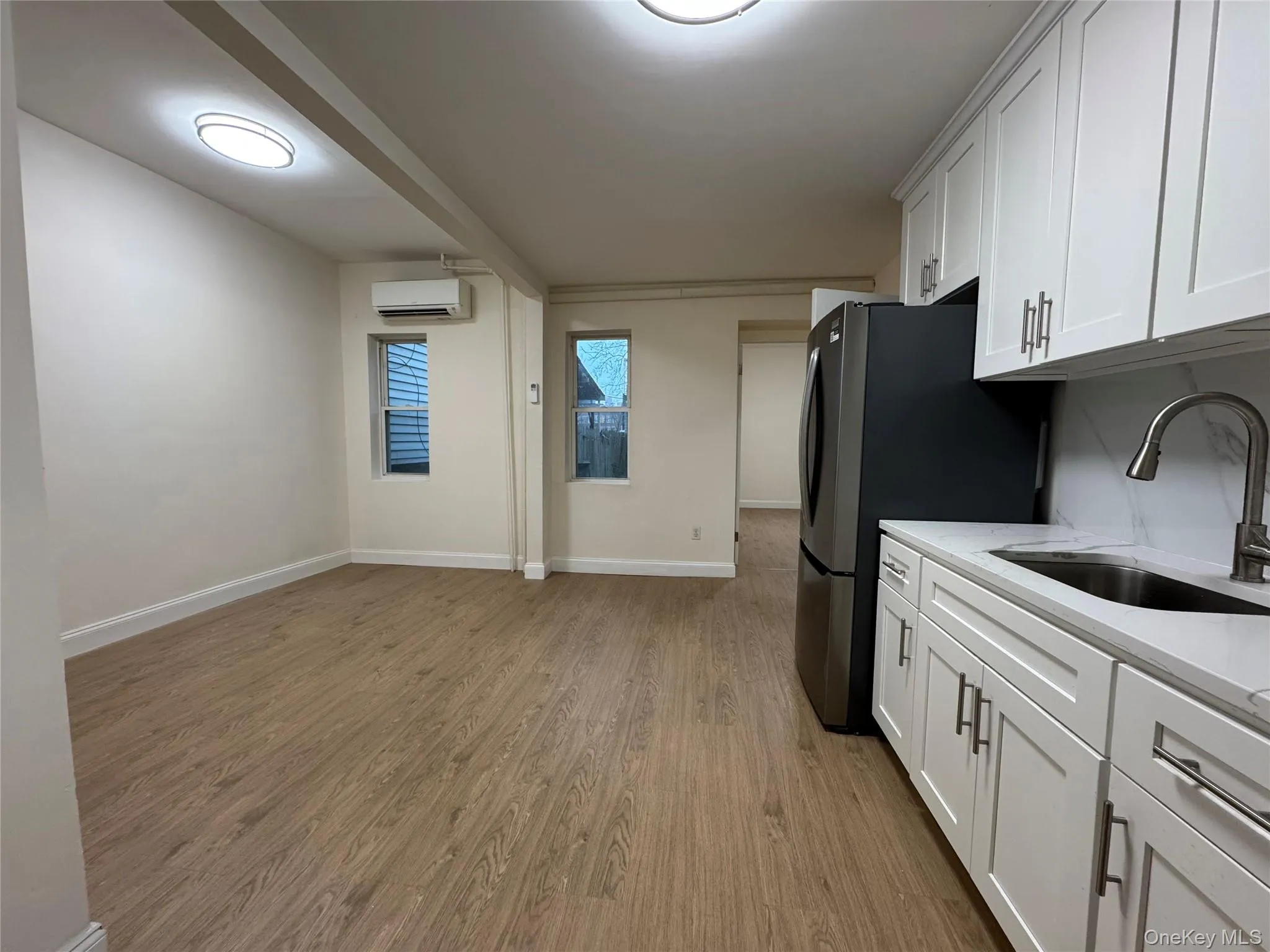 Kitchen with white cabinetry, light stone counters, light wood finished floors, and freestanding refrigerator Kitchen with white cabinetry, light stone counters, light wood finished floors, and freestanding refrigerator