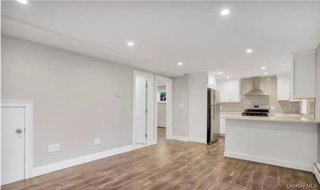 Kitchen with kitchen peninsula, stainless steel appliances, dark wood-type flooring, wall chimney range hood, and white cabinets Kitchen with kitchen peninsula, stainless steel appliances, dark wood-type flooring, wall chimney range hood, and white cabinets