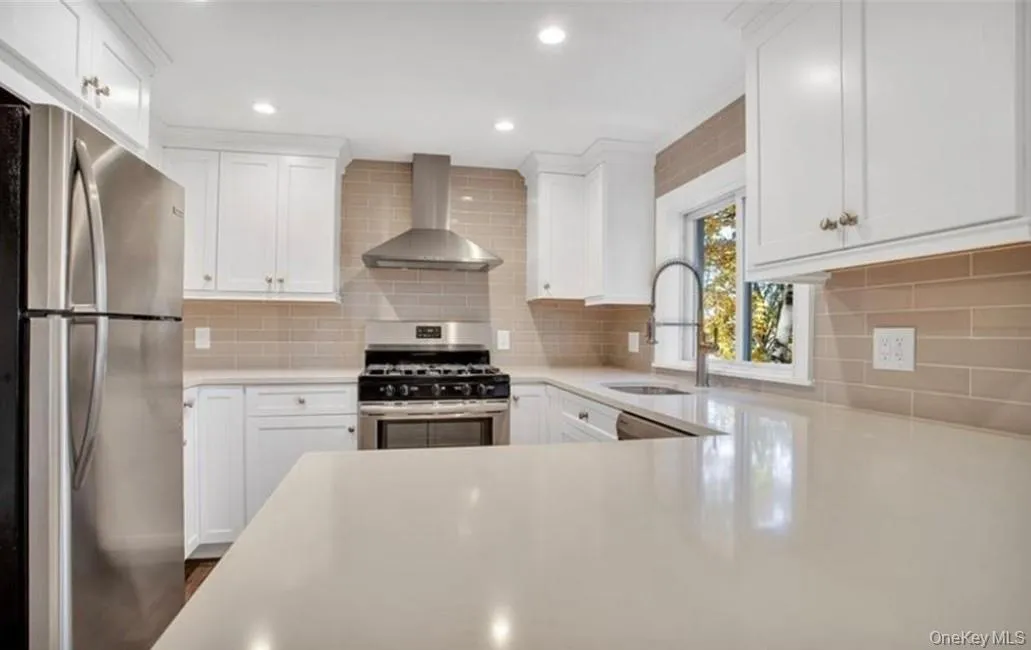 Kitchen with white cabinets, wall chimney exhaust hood, and stainless steel appliances Kitchen with white cabinets, wall chimney exhaust hood, and stainless steel appliances
