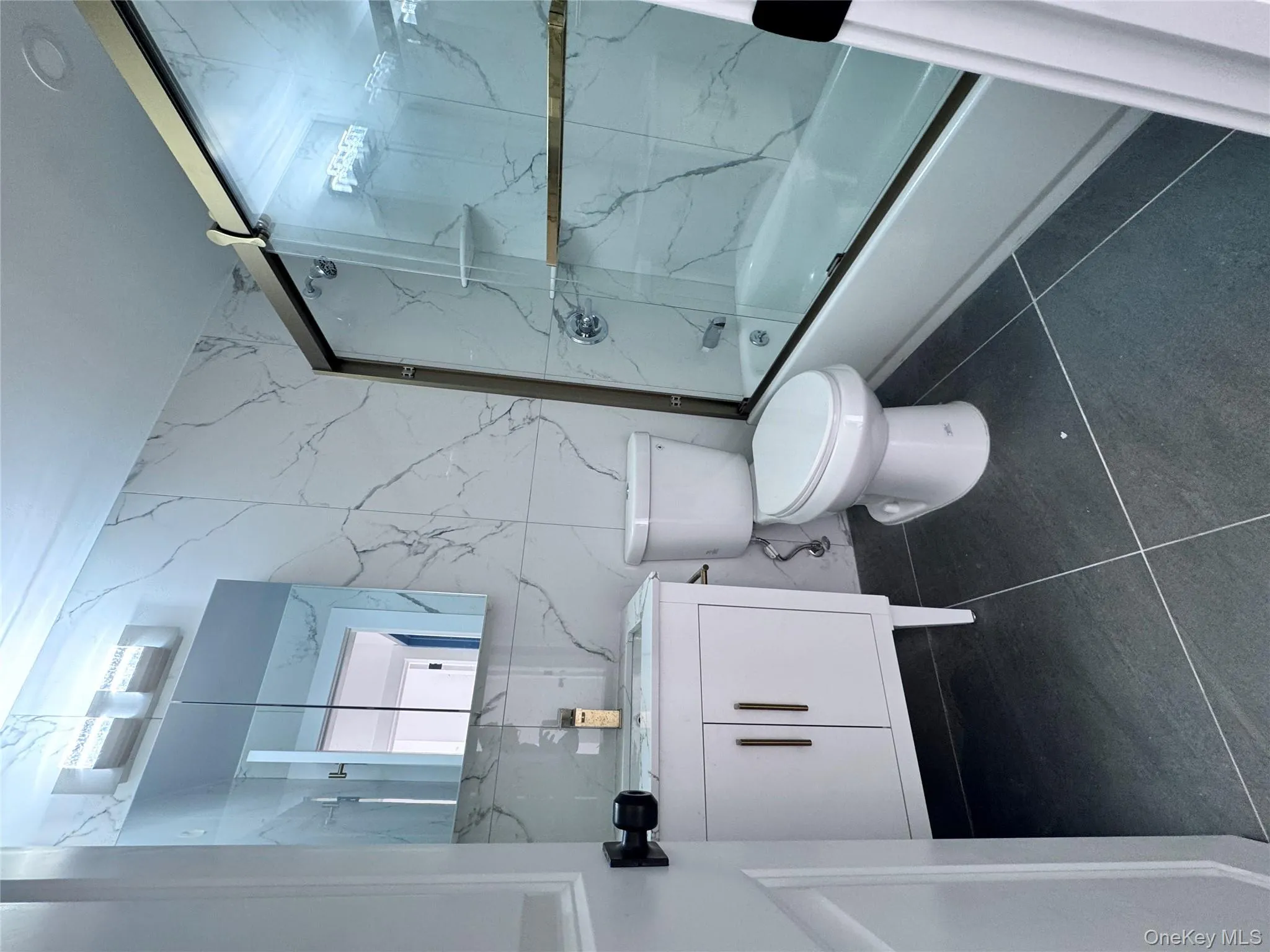 Bathroom featuring vanity, bath / shower combo with glass door, dark tile patterned flooring, tile walls, and stone wall Bathroom featuring vanity, bath / shower combo with glass door, dark tile patterned flooring, tile walls, and stone wall