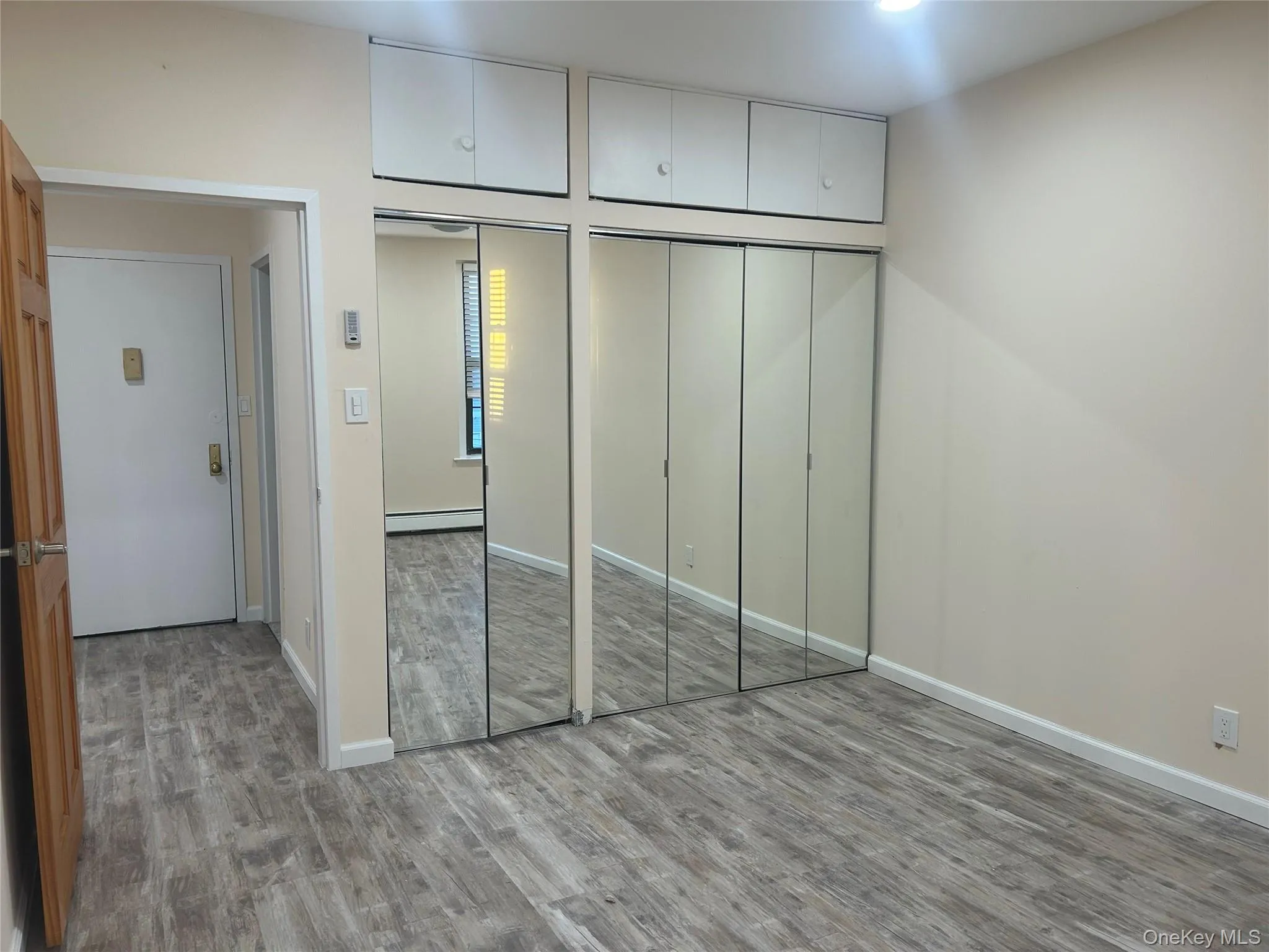 Unfurnished bedroom featuring multiple closets, wood finished floors, and baseboard heating Unfurnished bedroom featuring multiple closets, wood finished floors, and baseboard heating