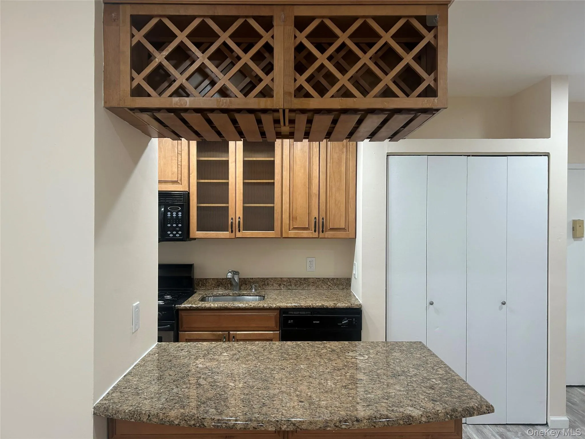 Kitchen with dark stone counters, black appliances, brown cabinetry, and glass insert cabinets Kitchen with dark stone counters, black appliances, brown cabinetry, and glass insert cabinets