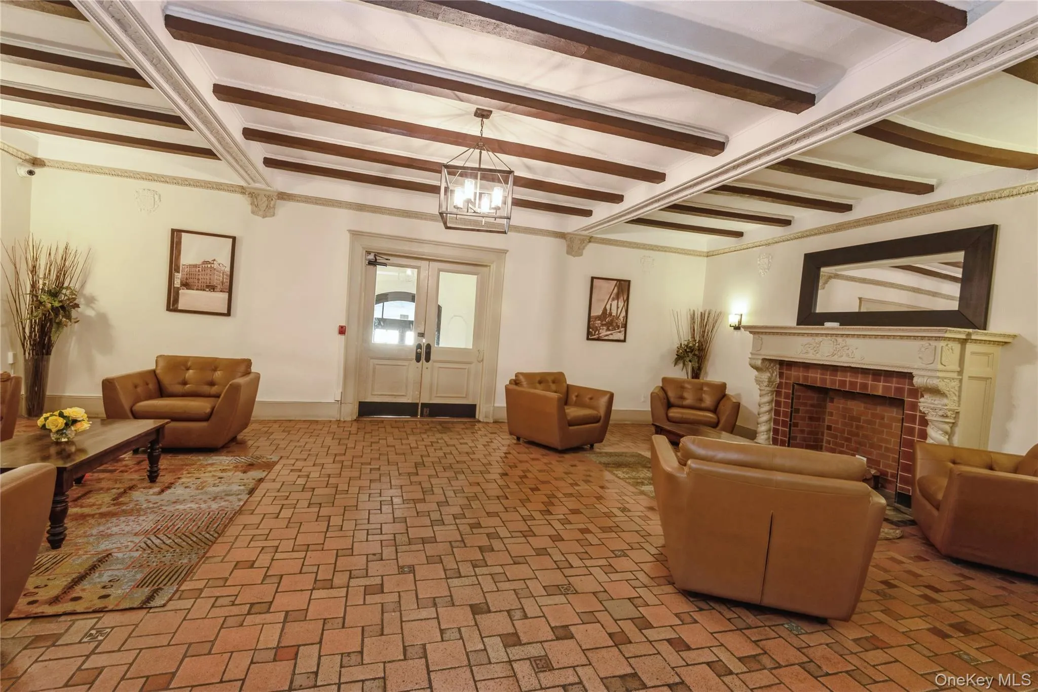 Living room with beamed ceiling, brick patterned floors, a fireplace, and a chandelier Living room with beamed ceiling, brick patterned floors, a fireplace, and a chandelier