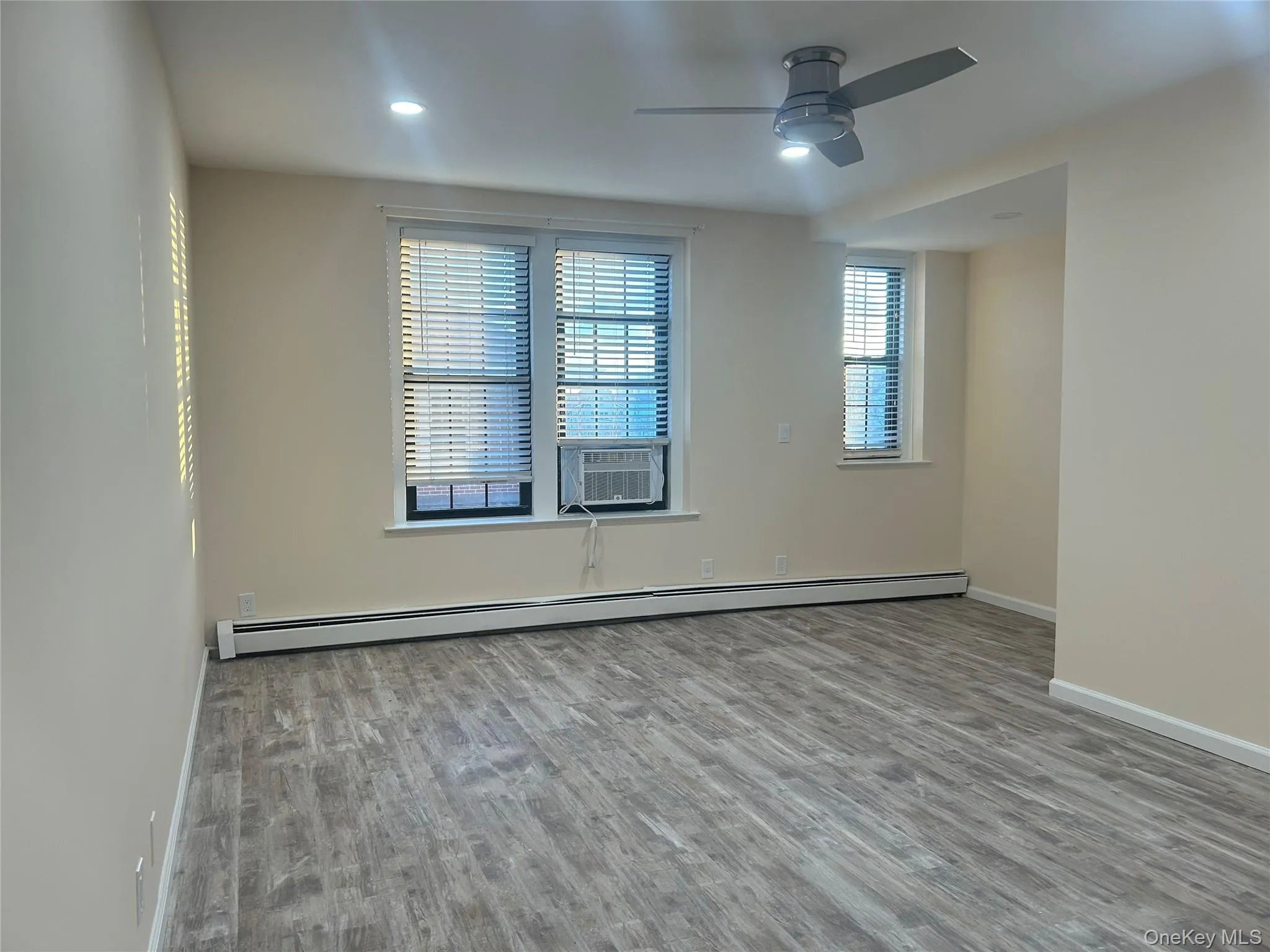 Empty room with a baseboard heating unit, wood finished floors, a ceiling fan, recessed lighting, and cooling unit Empty room with a baseboard heating unit, wood finished floors, a ceiling fan, recessed lighting, and cooling unit