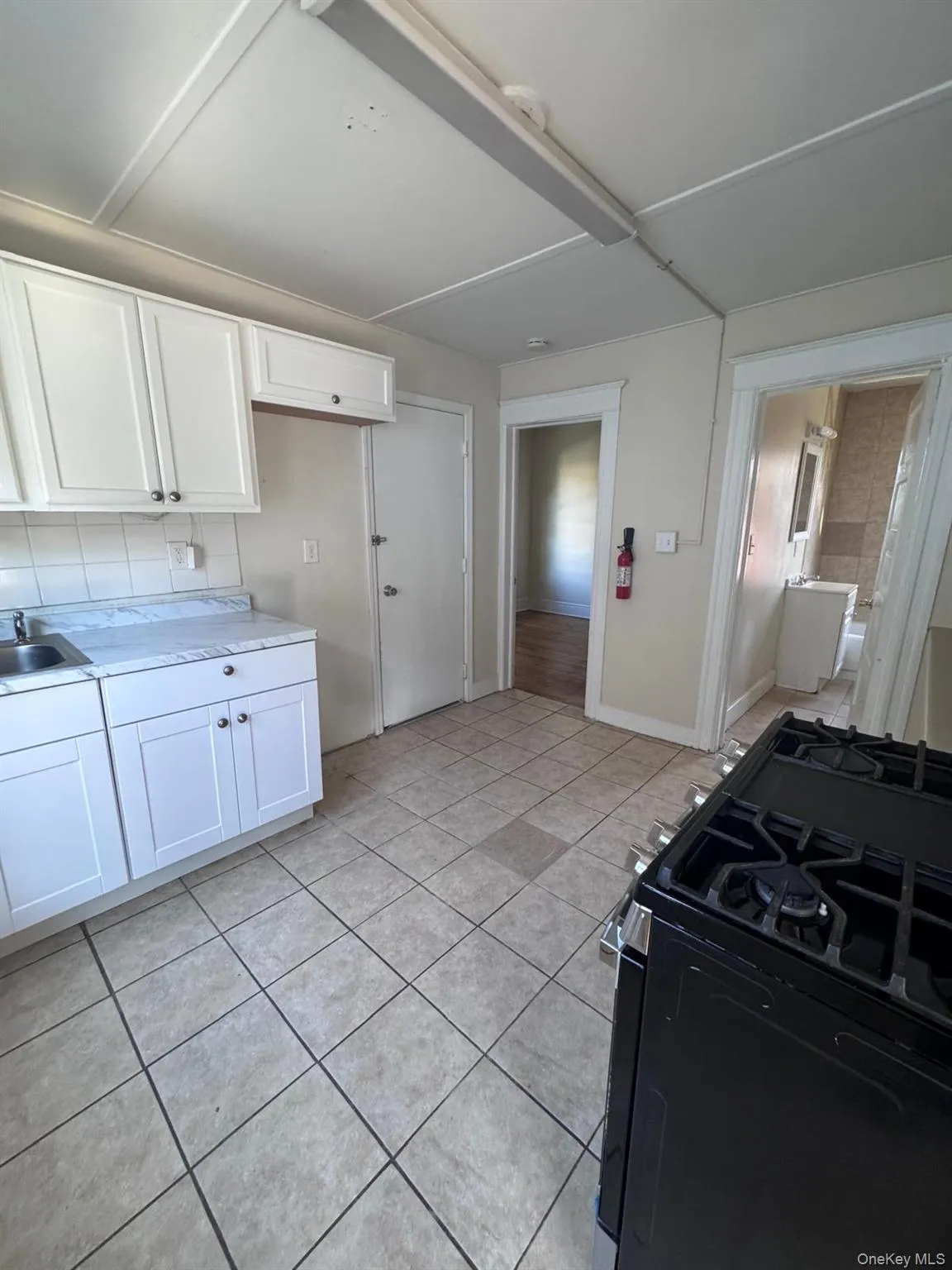 Kitchen with gas stove, white cabinetry, light countertops, decorative backsplash, and light tile patterned flooring Kitchen with gas stove, white cabinetry, light countertops, decorative backsplash, and light tile patterned flooring