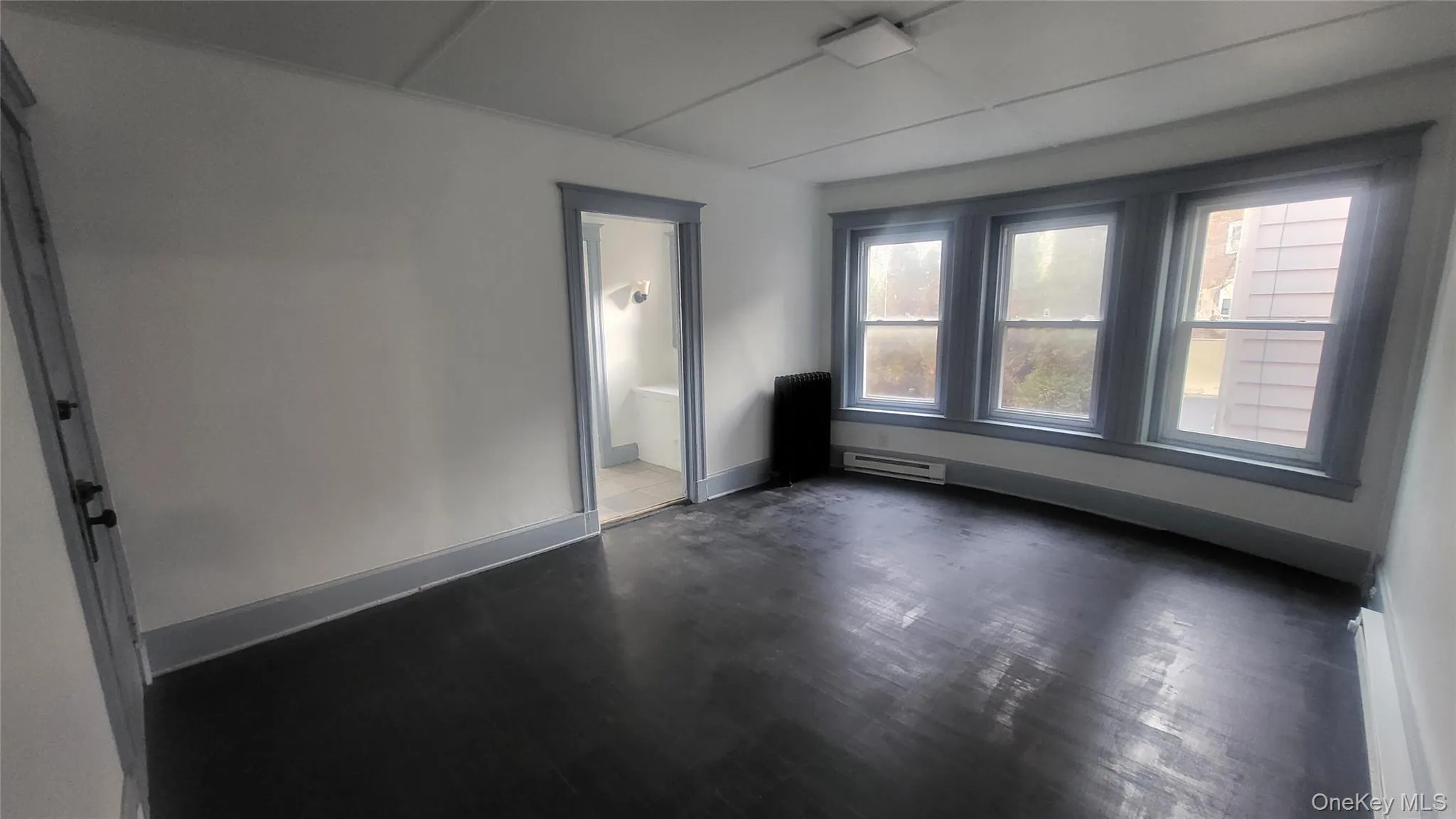 Unfurnished room with a baseboard heating unit, radiator, and dark wood-style flooring Unfurnished room with a baseboard heating unit, radiator, and dark wood-style flooring