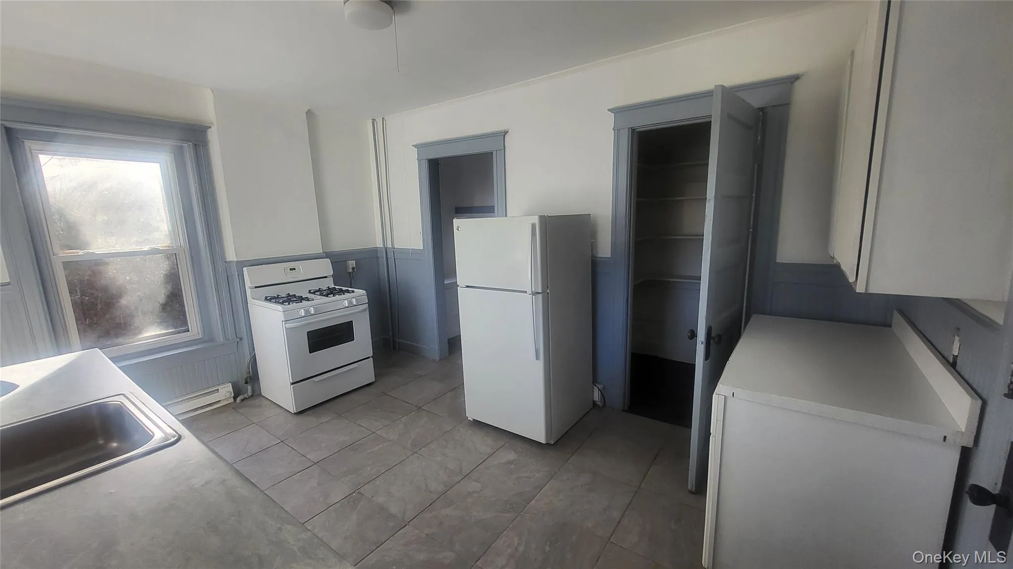 Kitchen featuring a wainscoted wall, white appliances, light countertops, a baseboard heating unit, and white cabinetry Kitchen featuring a wainscoted wall, white appliances, light countertops, a baseboard heating unit, and white cabinetry
