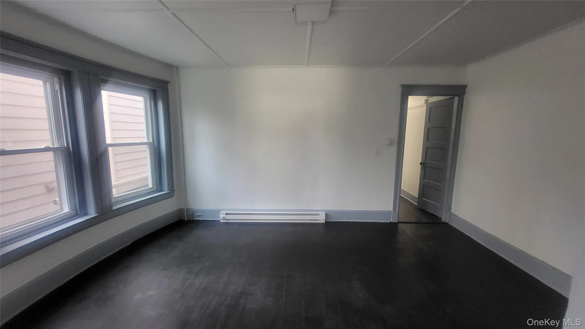 Unfurnished room featuring dark wood-style floors and baseboard heating Unfurnished room featuring dark wood-style floors and baseboard heating