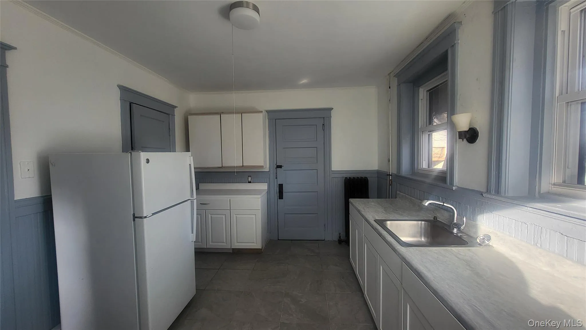 Kitchen with a wainscoted wall, freestanding refrigerator, light countertops, white cabinets, and radiator heating unit Kitchen with a wainscoted wall, freestanding refrigerator, light countertops, white cabinets, and radiator heating unit