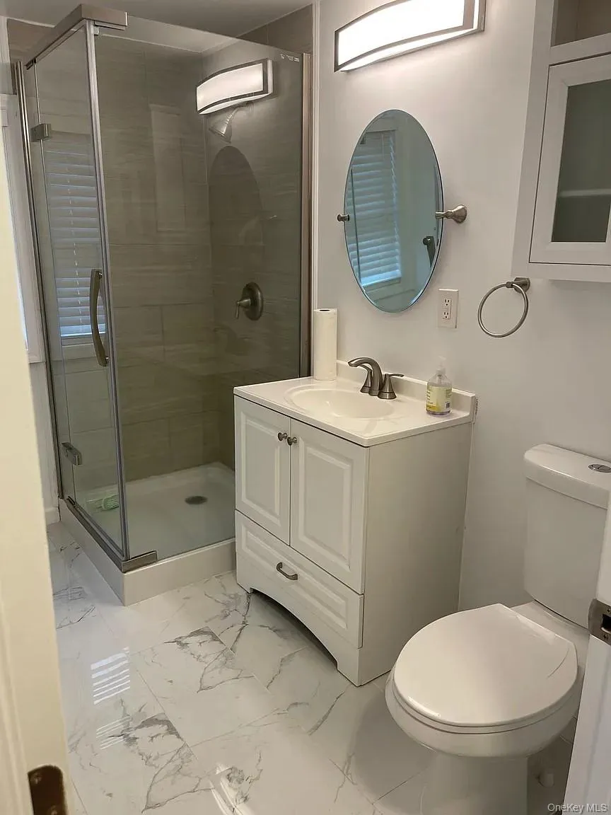 Bathroom featuring a stall shower, vanity, and light marble finish floors Bathroom featuring a stall shower, vanity, and light marble finish floors