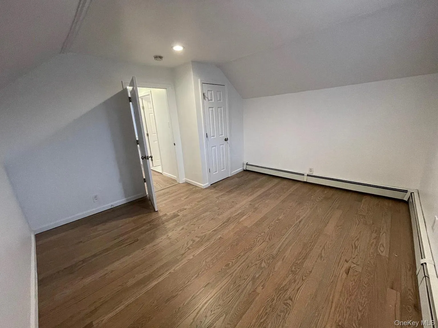 Additional living space featuring lofted ceiling, a baseboard radiator, and wood finished floors Additional living space featuring lofted ceiling, a baseboard radiator, and wood finished floors