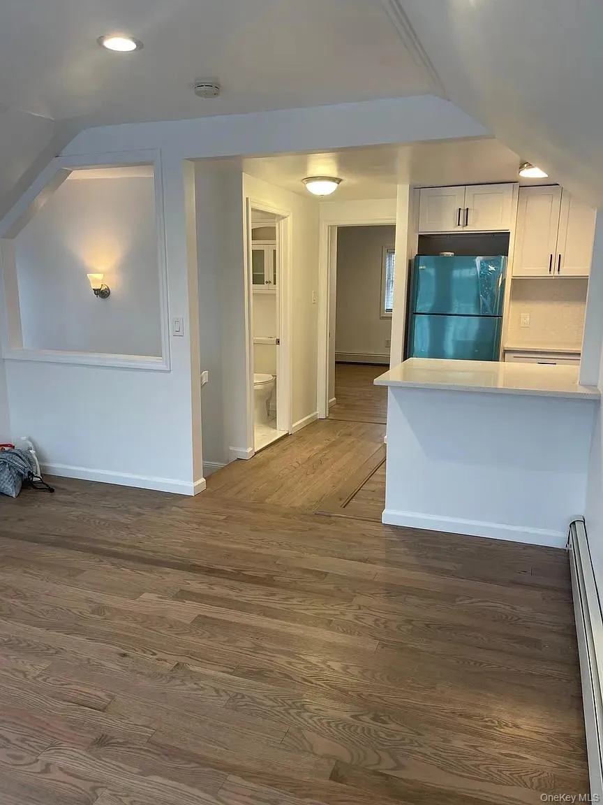 Kitchen with freestanding refrigerator, white cabinetry, a baseboard heating unit, dark wood-type flooring, and light stone counters Kitchen with freestanding refrigerator, white cabinetry, a baseboard heating unit, dark wood-type flooring, and light stone counters