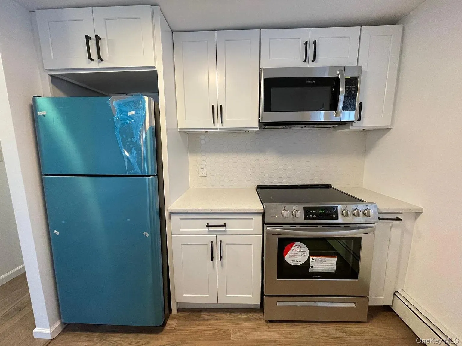 Kitchen featuring white cabinets, stainless steel appliances, a baseboard heating unit, and light wood finished floors Kitchen featuring white cabinets, stainless steel appliances, a baseboard heating unit, and light wood finished floors