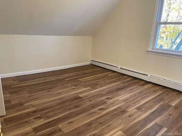 Bonus room featuring dark wood-style floors, a baseboard radiator, and lofted ceiling Bonus room featuring dark wood-style floors, a baseboard radiator, and lofted ceiling
