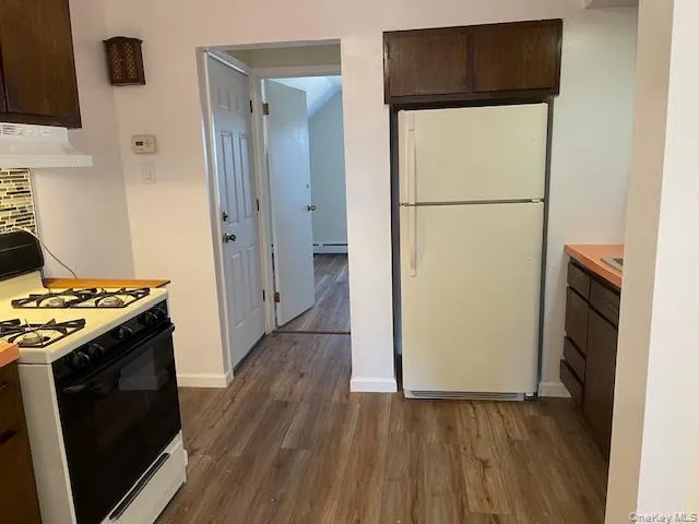 Kitchen featuring dark brown cabinetry, white appliances, and dark wood-style floors Kitchen featuring dark brown cabinetry, white appliances, and dark wood-style floors
