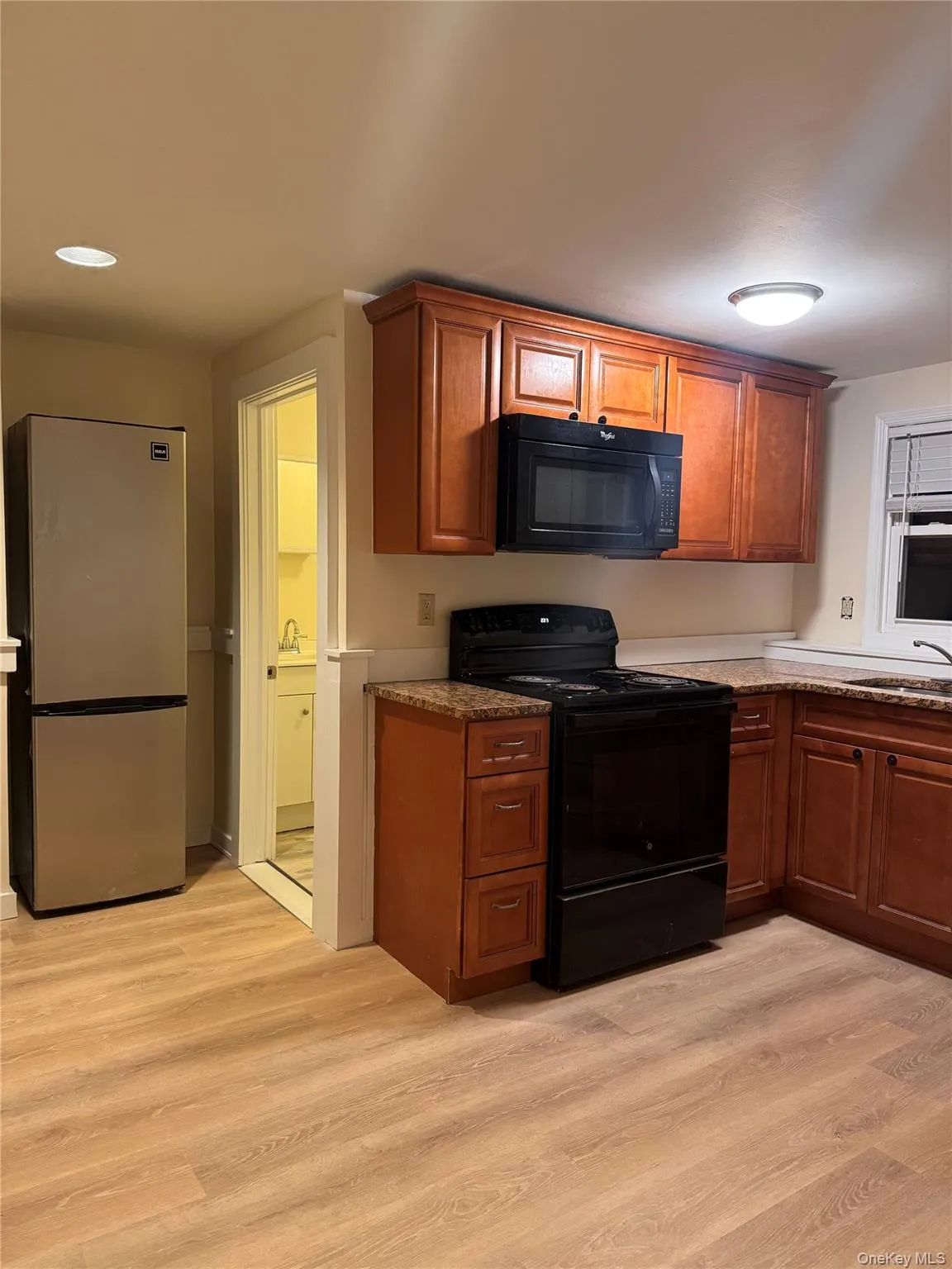 Kitchen featuring black appliances, brown cabinetry, light wood finished floors, and dark stone counters Kitchen featuring black appliances, brown cabinetry, light wood finished floors, and dark stone counters