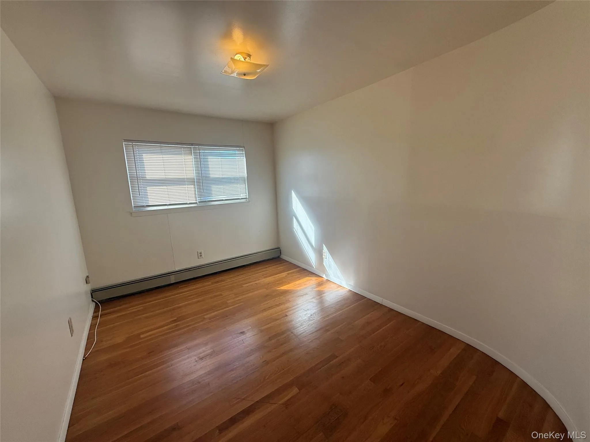 Unfurnished room featuring a baseboard heating unit and light wood finished floors Unfurnished room featuring a baseboard heating unit and light wood finished floors